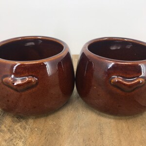 Peut inclure: Deux bols en céramique marron avec une petite lèvre surélevée à l'avant. Les bols sont émaillés et ont une finition brillante.