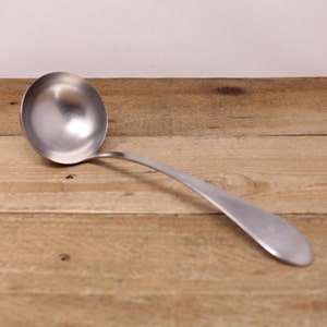 May include: A silver ladle with a long handle. The ladle is resting on a wooden surface.