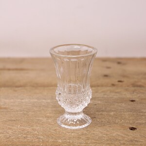 Peut inclure: Un petit verre transparent avec un motif décoratif et texturé. Le verre a un dessus évasé, une base à motifs et un petit pied rond. Le verre est probablement utilisé pour servir une petite quantité de liquide.