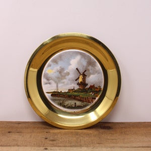 Peut inclure: Une assiette décorative encadrée de laiton avec une scène peinte d'un moulin à vent dans un paysage hollandais.
