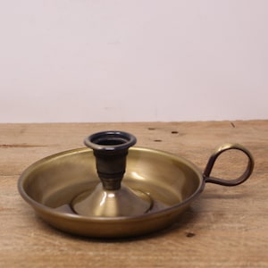 Peut inclure: Un bougeoir en laiton vintage avec une base circulaire et une poignée. Le support a un intérieur bleu foncé et une pointe centrale pour fixer une bougie. Le laiton a une patine chaude et vieillie, suggérant qu'il s'agit d'une antiquité. Diamètre: environ 15 cm.