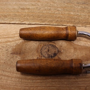 May include: Two vintage wooden handled bottle openers with a silver, wavy metal opener. The openers are on a wooden surface.