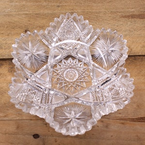 May include: A clear glass bowl with a starburst pattern. The bowl is made of cut glass and has a scalloped edge.