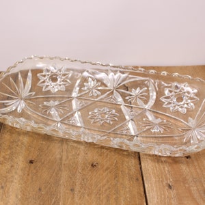 May include: A clear glass serving dish with a scalloped edge and a geometric starburst pattern.