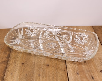 May include: A clear glass serving dish with a scalloped edge and a geometric starburst pattern.