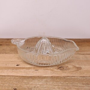 May include: Clear glass citrus juicer with a ribbed bowl and a central reamer. The juicer has a handle and a spout for easy pouring. A kitchen tool for squeezing fresh juice.