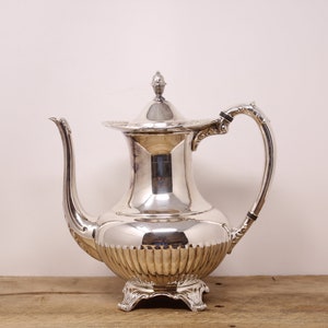May include: A silver teapot with a fluted body and a decorative handle. The teapot has a lid with a finial on top.