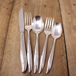 May include: A set of five silver-plated cutlery pieces, including a knife, two forks, and two spoons, laid out on a wooden surface.