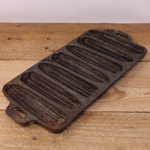 Peut inclure: Un moule à pain de maïs en fonte vintage avec six moules individuels. Le moule est gris foncé et a un aspect rustique et usé.