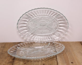 May include: Two clear glass serving dishes with four divided sections. The dishes have a raised, textured design around the edges and in the center.