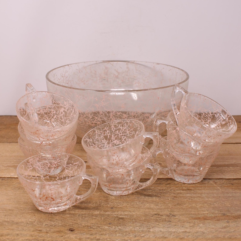May include: A vintage glass punch bowl and cups set with a crackle finish. The bowl and cups are clear glass with a delicate pink crackle pattern.