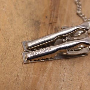 May include: Close-up of two silver metal clips with the text "PAT. 2435761" engraved on each. The clips are attached to a pearl necklace.