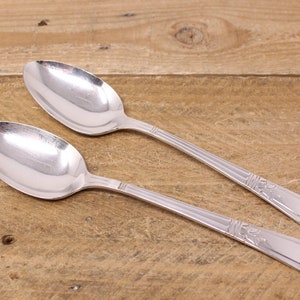 May include: Two silver spoons with ornate designs on a wooden surface.