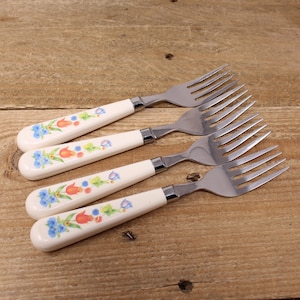 May include: Four stainless steel forks with white handles featuring a floral design in shades of blue, orange, and green.