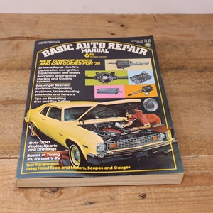 May include: A yellow car with the hood open, revealing the engine. The book cover is for a 6th edition auto repair manual, titled "Basic Auto Repair Manual" with the subtitle "New Tune-Up Specs and Car Guides for '74".