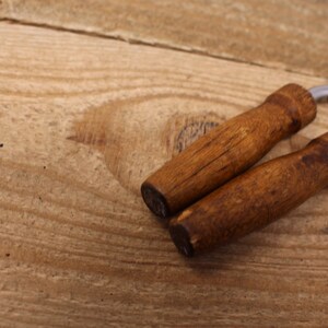 May include: Two wooden handled metal meat forks on a wooden surface.