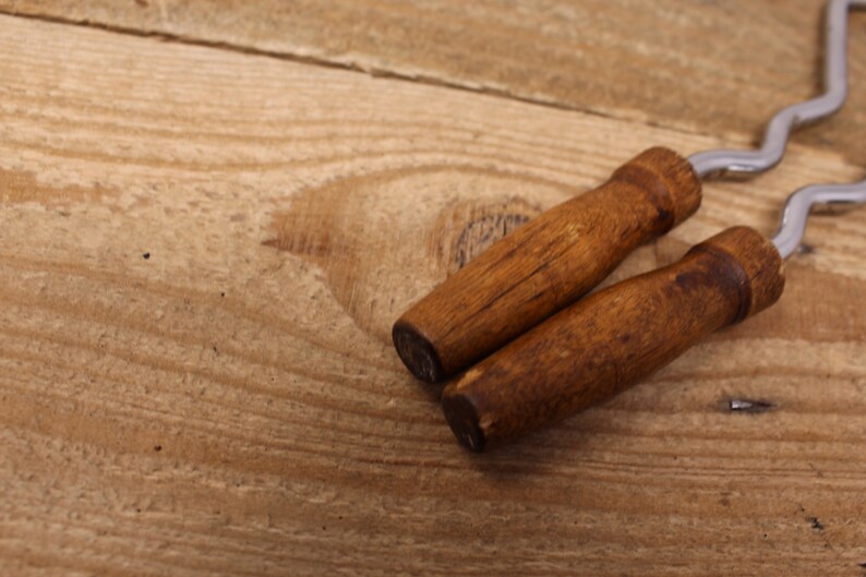 May include: Two wooden handled metal meat forks on a wooden surface.