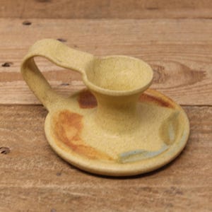 May include: A yellow ceramic candle holder with a handle and a brown and blue glaze.