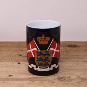 May include: A blue and white ceramic vase featuring a Danish coat of arms with a crown, three lions, and the word "DANMARK".