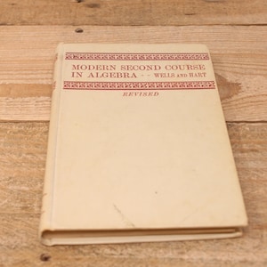 May include: A vintage book titled "Modern Second Course in Algebra - Wells and Hart" with a red border and the word "Revised" printed on the cover.