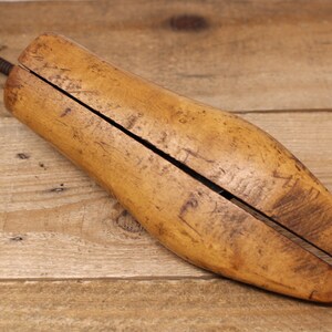 May include: A wooden shoe stretcher with a metal screw mechanism. The stretcher is made of light brown wood and has a split design to fit inside a shoe.