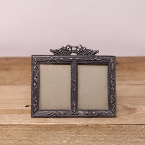 May include: A silver-toned double picture frame with a decorative floral design. The frame has two openings for photos.