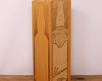 May include: A wooden box with a carved bottle silhouette on the left side. The right side features a detailed label with the text "Sleeman Sparkling Ale" and a bottle illustration. The box is made of light-colored wood.