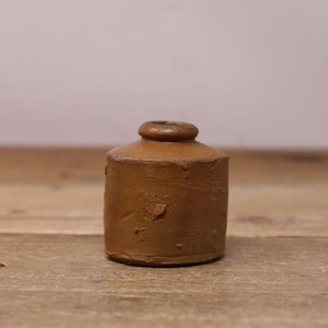 May include: A small, brown, ceramic inkwell with a rounded shape and a slightly uneven surface.