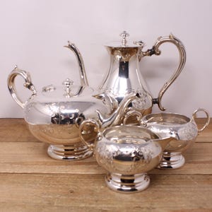 May include: A silver tea set with a teapot, creamer, and sugar bowl. The set has an ornate design with floral patterns.
