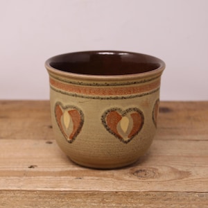 May include: A brown ceramic planter with a beige glaze and three stylised heart designs in orange and beige.