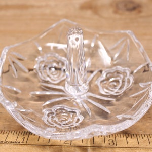May include: A clear glass ring holder with a raised center and three etched rose designs.