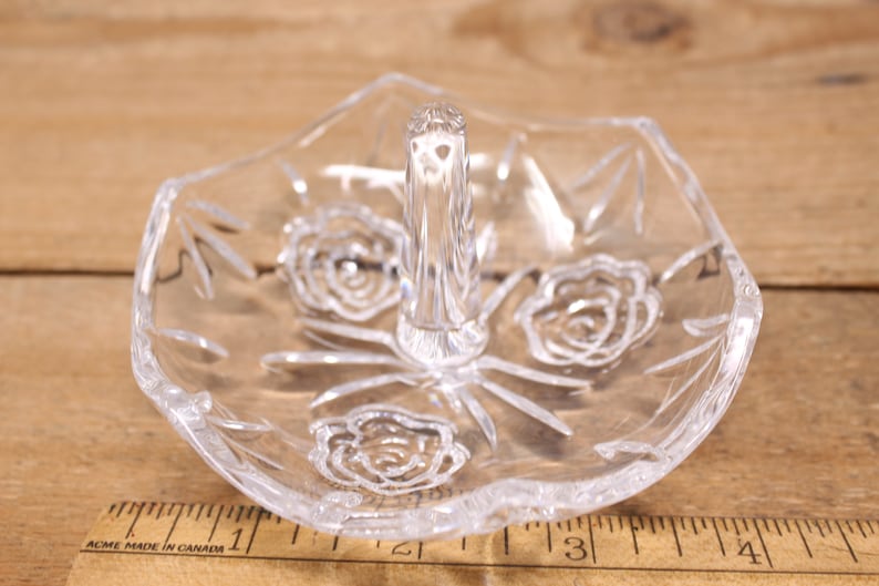 May include: A clear glass ring holder with a raised center and three etched rose designs.