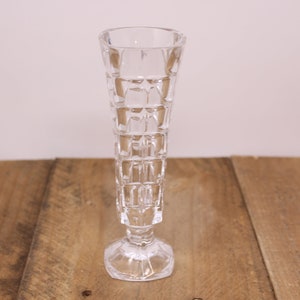 May include: A clear glass vase with a geometric pattern. The vase has a tall, slender shape with a wide base.