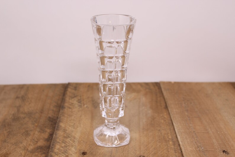 May include: A clear glass vase with a geometric pattern. The vase has a tall, slender shape with a wide base.