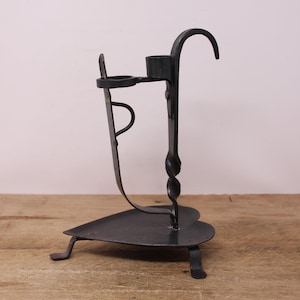 May include: Black metal candle holder with a heart-shaped base and a twisted stem. The holder has a single candle cup and a hook on the top.