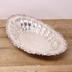 May include: A silver oval serving tray with a decorative, scalloped edge. The tray has a slightly raised centre and a smooth, polished surface.