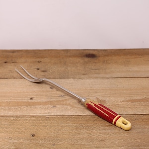 May include: A red and yellow handled metal fork with two prongs. The fork is lying on a wooden surface.