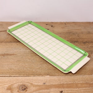 May include: A rectangular serving tray with a green border and a grid pattern. The tray features a cream-coloured surface with a green grid design and black trim. It has small handles at each end. The tray is likely ceramic.