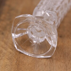 May include: A clear glass vase with a textured, geometric pattern. The vase has a wide, circular base.