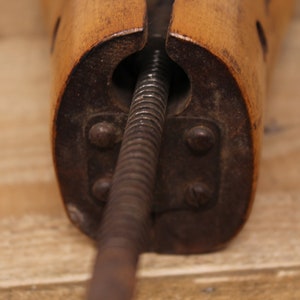 May include: Close-up of a wooden shoe stretcher with a metal screw mechanism. The stretcher is made of light brown wood and has a dark brown metal screw.