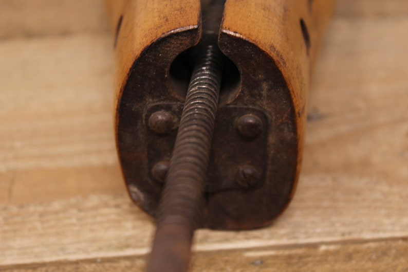 May include: Close-up of a wooden shoe stretcher with a metal screw mechanism. The stretcher is made of light brown wood and has a dark brown metal screw.