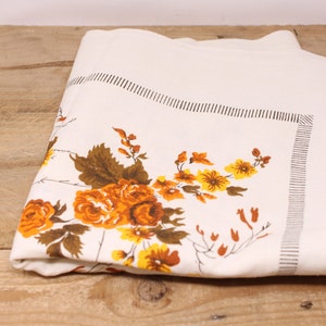 May include: White tablecloth with a brown and yellow floral pattern. The tablecloth has a brown border with a repeating pattern of small lines.