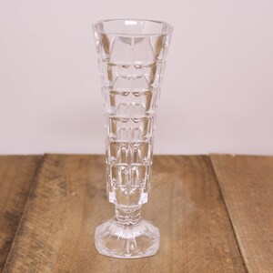 May include: A clear glass vase with a geometric pattern. The vase has a wide base and a narrow neck.
