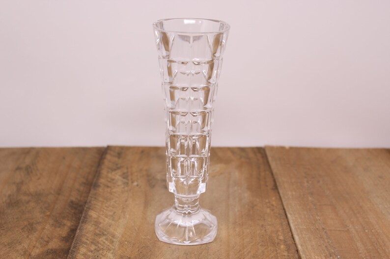 May include: A clear glass vase with a geometric pattern. The vase has a wide base and a narrow neck.