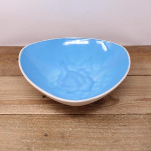 May include: A ceramic bowl with a light blue interior and a white rim. The bowl has an organic, asymmetrical shape and sits on a wooden surface. The bowl is empty and ready to be filled.