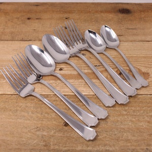 May include: A set of seven silver-toned cutlery pieces, including forks and spoons, arranged on a wooden surface.