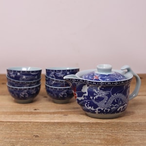 May include: A blue and white ceramic tea set featuring a teapot with a dragon design and six matching teacups. The teapot has a curved handle and spout. The teacups and teapot have a blue and white wave pattern.
