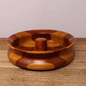 Peut inclure: Un bol rond en bois présentant un motif segmenté alternant des tons de bois brun clair et foncé. Le bol possède une finition lisse et polie ainsi qu'un pilier central surélevé avec quatre petits trous sur le dessus, formant un bassin circulaire.