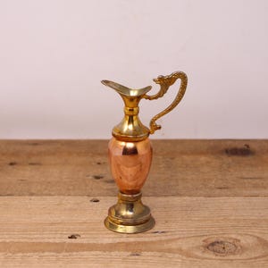 May include: A small decorative pitcher. The body is copper, and the top, base, and handle are brass. The handle has a dragon-like design. The pitcher's height is approximately 15 cm.