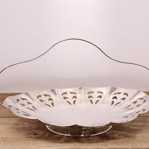 May include: A silver serving dish with a scalloped edge and a decorative cut-out design. The dish has a handle and a pedestal base.